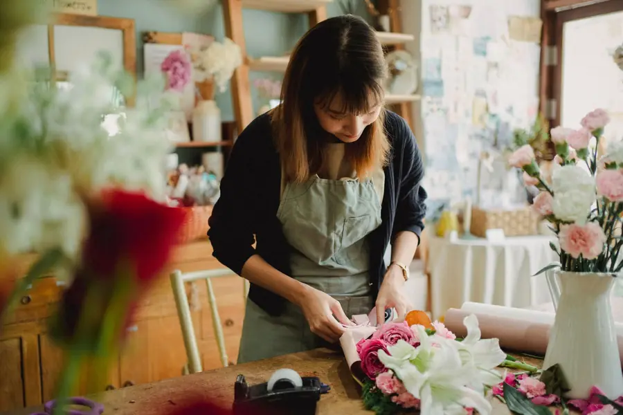 A florist wrapping a bouquet in paper at the counter